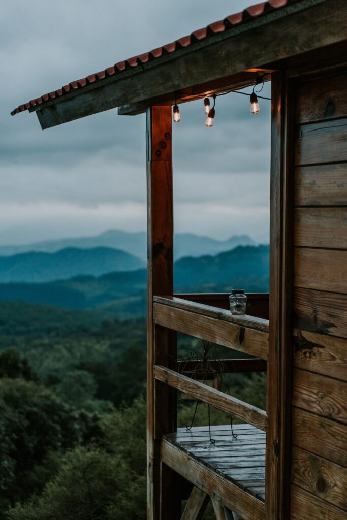 Wooden cabin porch with warm lights overlooking layered mountain ridges