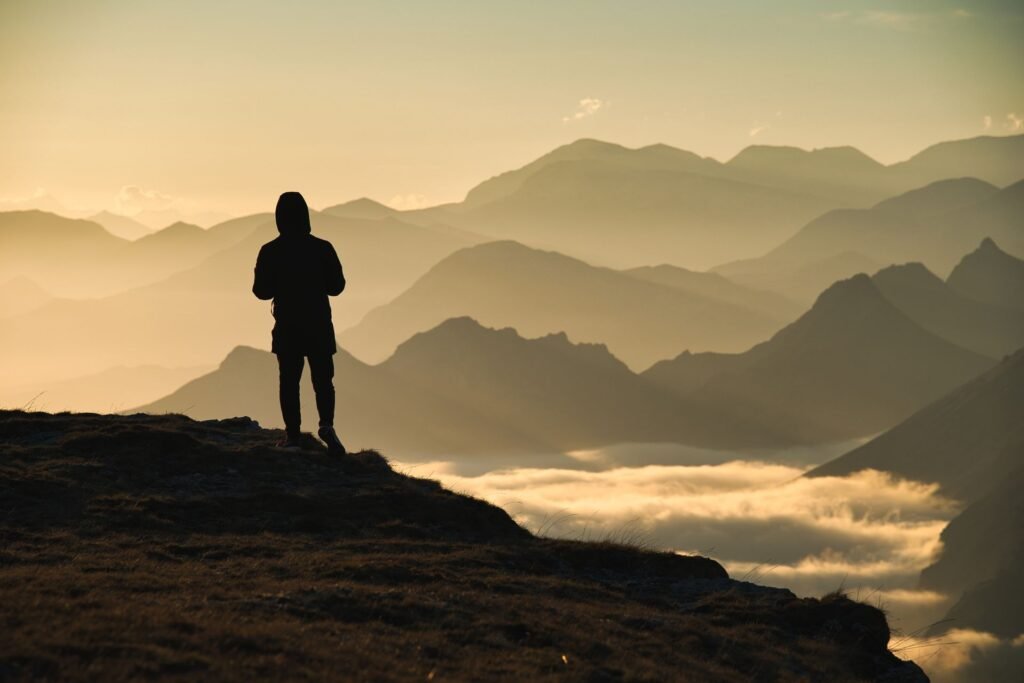 Silhouette of a hiker standing on a mountain summit above clouds at dawn