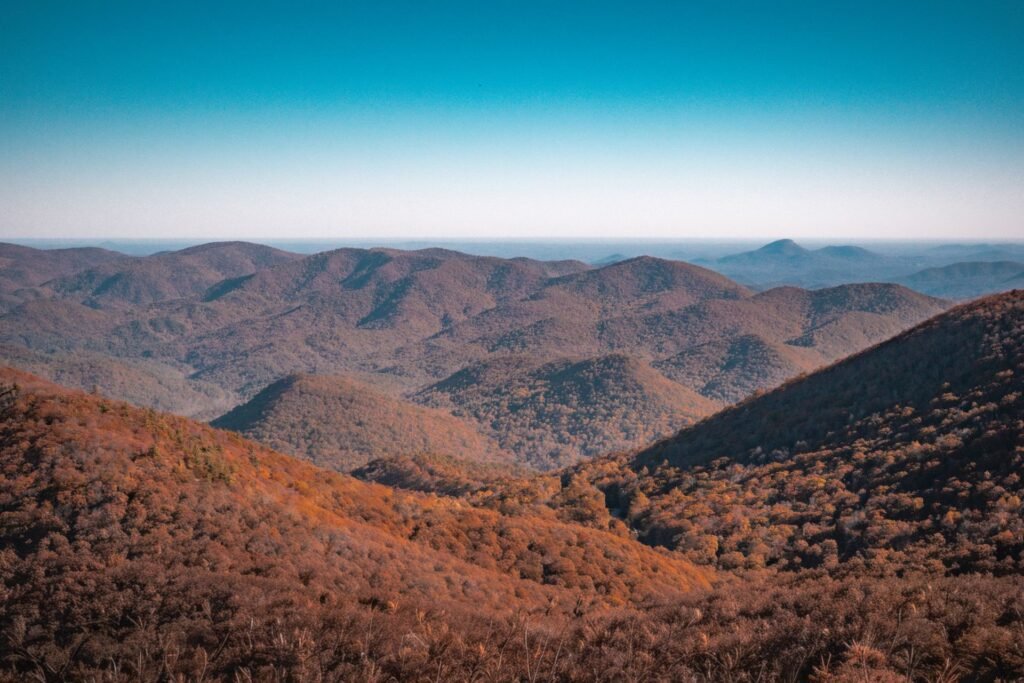 Layered mountain ridges covered in russet and orange autumn foliage under a clear blue sky